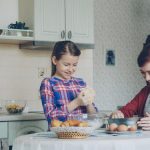 Little cute girl helping her mother in the kitchen stirring dough for cookies into bowl. Mom have fun smearing daughter nose with flour and they laughing . Family, food, home and people concept
